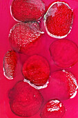 Slices of cut fresh beetroot arranged on wet bright fuchsia surface as abstract background