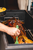 Crop faceless cook smearing sauce with brush on roasted suckling lamb grilling on metal rack in cafe during cooking process