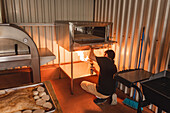 Back view of anonymous male worker warming up modern roasting oven with gas burner in kitchen with uncooked pork during work in cafe