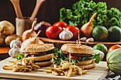Appetitliche Hamburger mit Gemüse und Schnitzel auf einem Holzbrett mit Pommes frites in der Küche