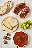 Top view arrangement of plates with appetizing sliced wurst and cheese served on plank table near sweet grape and bread
