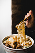 Hand with chopsticks pulling noodles while eating beef noodles soup from big ceramic bowl