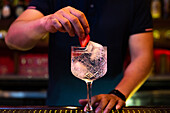 Unbekannter Barkeeper dekoriert einen Gin-Tonic-Cocktail mit einer Erdbeere in der Bar