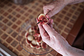 From above of crop unrecognizable elderly person with knife cutting ripe fig above bowl on table in house