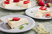 Slices of tasty sweet baked cheesecake with ripe strawberries served on white plates on table in light kitchen