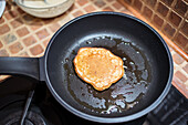 Delicious homemade pancake on frying pan with oil on stove near glass bowl in kitchen