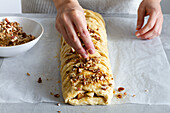 From above of crop anonymous female chef putting crunchy nut pieces on top of apple pastry on baking paper