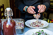 Unkenntlich gemachter männlicher Koch in schwarzer Uniform mit Armbändern serviert köstlichen Salat auf einem Teller auf dem Küchentisch