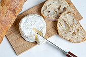 Von oben köstlicher Camembert-Käse auf hölzernem Schneidebrett neben Brotscheiben auf weißem Hintergrund