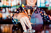 Anonymous cheerful female barkeeper with glass of refreshing vermouth standing at counter in bar