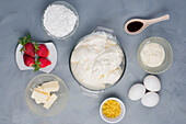 Draufsicht auf eine Schüssel mit Frischkäse in der Nähe von Eiern und Butter auf einem Tisch mit Erdbeeren und Vanilleextrakt zum Backen von Käsekuchen
