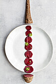 Overhead creative composition of sweet beet slices arranged in line on white plate with vegetable root and tail on sides