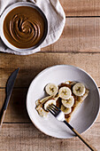 From above silverware placed near yummy crepes with sweet nut butter and slices of banana on wooden table