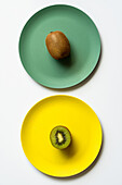 Blick von oben auf frische reife halbierte und ganze Kiwis, die auf gelben und grünen Tellern auf einem weißen Tisch serviert werden