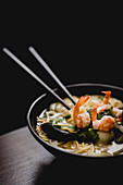 Bowl of tasty oriental noodle soup with fresh prawns placed on table against black background