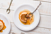Top view of fresh egg custard topped with sweet dulce de leche served with syrup on wooden table with cutlery in kitchen