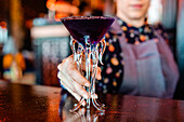 Anonymous female barkeeper standing at bar counter with a type of alcohol drink served in creative cocktail glasses in shape of jellyfish