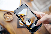 Crop anonymous female customer taking picture with mobile phone of beer and snacks in bar