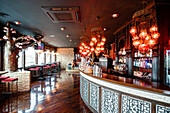 Cozy interior of spacious bar with wooden counter and tables illumined by glowing chandeliers