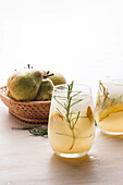 From above of cold pear cocktail in glasses with rosemary and ice cubes placed on table with fresh fruits