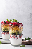 Appetitlicher Joghurt mit Schichten von frischen Früchten, serviert in Gläsern auf einem Tisch mit Minzblättern