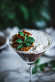 Glas süßes Mousse mit Schokolade und Kokosnuss, garniert mit Minzblättern und auf einem Tisch mit Grünpflanzen platziert