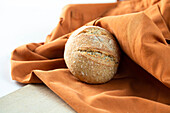 Loaf of tasty fresh bread placed on orange fabric in bakery