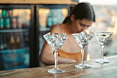 Busy female bartender working at counter with row of glasses with ice cubes in bar
