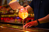 Hands of unrecognizable bartender putting ice cubes into the glass while preparing grapefruit and gin cocktail in the bar