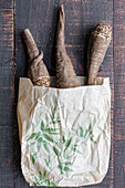 Top view composition of fresh raw beetroots in craft bag placed on shabby wooden table
