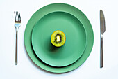 From above of half of fresh ripe juicy kiwi placed on green ceramic plates on white surface