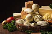 Collection of Italian cheese on table with fresh vegetables and curly parsley with basil leaves on spatulas