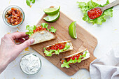 Kleine leckere Tacos mit rotem Kaviar und grünem Salat, serviert auf einem hölzernen Schneidebrett auf dem Tisch