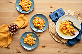 Draufsicht auf einen köstlichen frischen gesunden Salat mit reifen Kürbissen, roter Paprika und Kirschtomaten auf Tellern auf einem Holztisch in der Küche