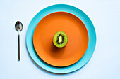 From above of half of fresh ripe juicy kiwi placed on orange and blue plates on white surface