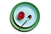 Draufsicht auf appetitliches rotes Beerengelee auf einem hellblauen runden Teller mit Löffel auf weißer Fläche