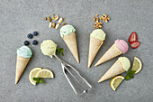 Top view of assorted appetizing ice cream cones with blueberry pistachio walnuts strawberry and lemon composed on gray table with ingredients in kitchen