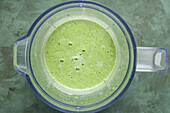 Draufsicht auf einen Mixer mit frischem Spinat, Eiweißpulver und Milch für die Zubereitung eines grünen Smoothies für die Keto-Diät