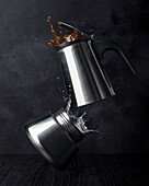Top view of stainless steel coffee maker with splattering water and hot drink on dark background