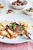 Leckere Crêpes mit Schokolade und Nüssen garniert, die auf einem Teller auf dem Tisch zum Frühstück serviert werden