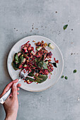 From above anonymous person with fork taking delicious lentil salad with cucumbers and spinach from plate over gray surface