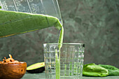 Nahaufnahme eines erfrischenden grünen Keto-Diät-Smoothies aus einer Mixerschüssel in ein Glas auf dem Tisch