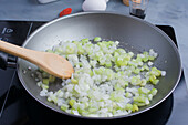 From above of chopped fresh green leek sauteing in oil on gray pan in kitchen