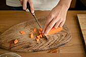 From above of crop unrecognizable chef cutting fresh carrot on wooden chopping board with knife while preparing healthy dish in kitchen