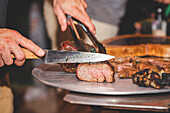 Anonymer männlicher Koch mit Zange, der gegrilltes Schweinefleisch auf einem Teller serviert, während er in der Nähe eines modernen Grills in einem Café steht