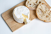 From above delicious camembert cheese placed on wooden chopping board near slices of bread on white background