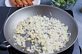 From above of fresh chopped onion in oil frying in pan on stove in kitchen