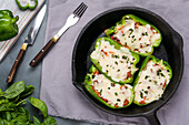 Halves of green bell pepper with pizza stuffing and melted cheese in skillet pan on table with green herbs in kitchen
