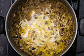 Draufsicht auf eine leckere hausgemachte Pilzsuppe, die in einem Topf auf einem modernen schwarzen Induktionsherd in einer hellen Küche kocht