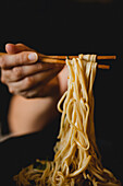 Hand of woman holding bamboo chopsticks with tasty wheat noodles from Chinese ramen meal plate